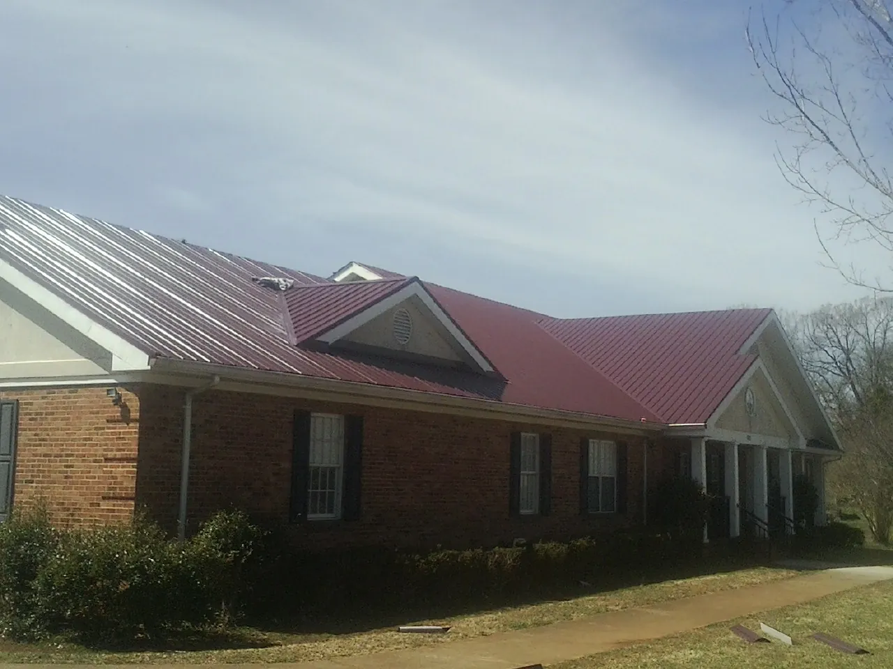 Red metal roof with gabled entries on a long brick building, from a Hail Damage Roof Repair job in Hardwick